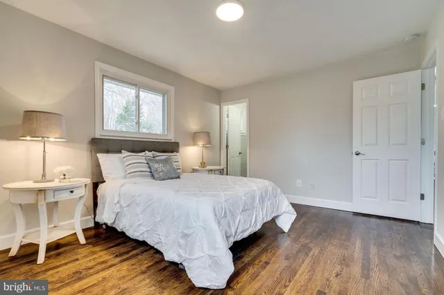 a bedroom with a bed and a lamp on dresser with wooden floor