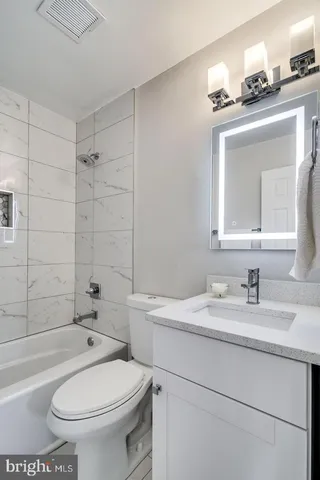 a bathroom with a granite countertop toilet a sink a mirror and bathtub