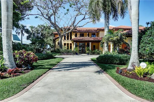 a front view of a house with a garden and palm trees