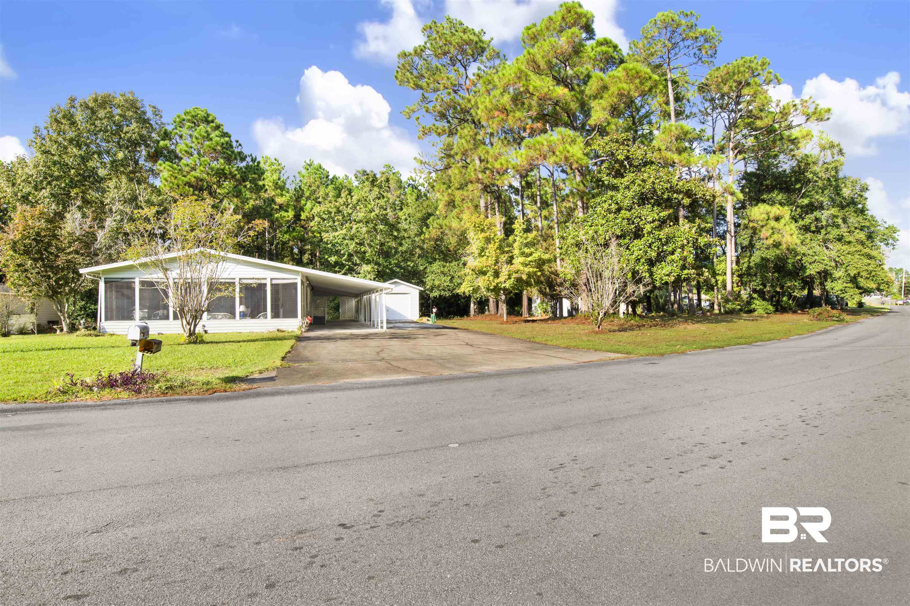 View of front facade featuring concrete driveway, a front yard, an attached carport, an outbuilding, and a sunroom