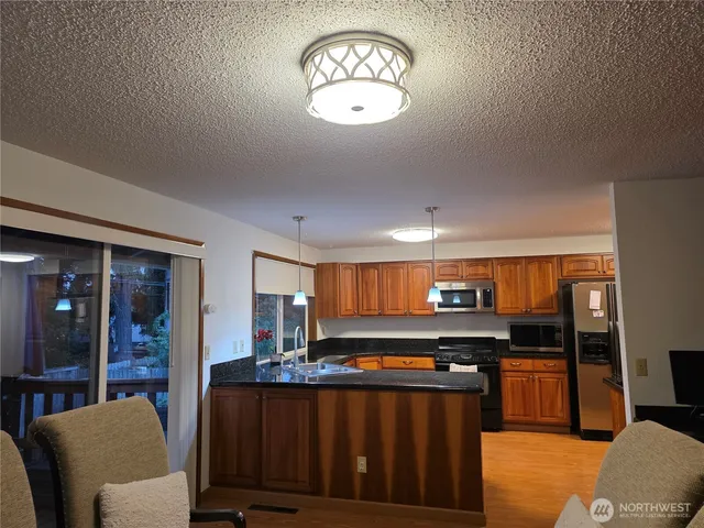 a kitchen with stainless steel appliances a stove a refrigerator a sink dishwasher and a dining table with wooden floor