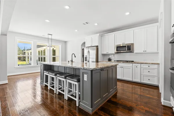 a kitchen with stainless steel appliances granite countertop a stove top oven a sink a refrigerator and white cabinets with wooden floor