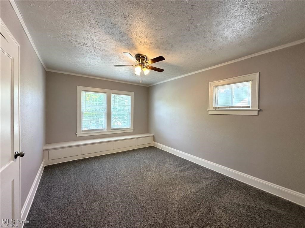 3277 Cedarbrook Road Cleveland, OH 44118 - Photo 10 of 18 Empty room with crown molding, healthy amount of natural light, a textured ceiling, dark carpet, and a ceiling fan