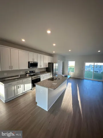 a large white kitchen with stainless steel appliances granite countertop a stove a sink a refrigerator and a wooden floors