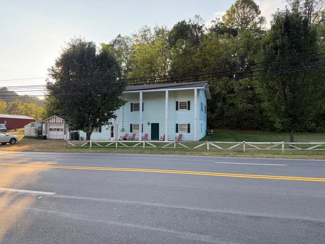 a view of a white house in a big yard with plants and large trees
