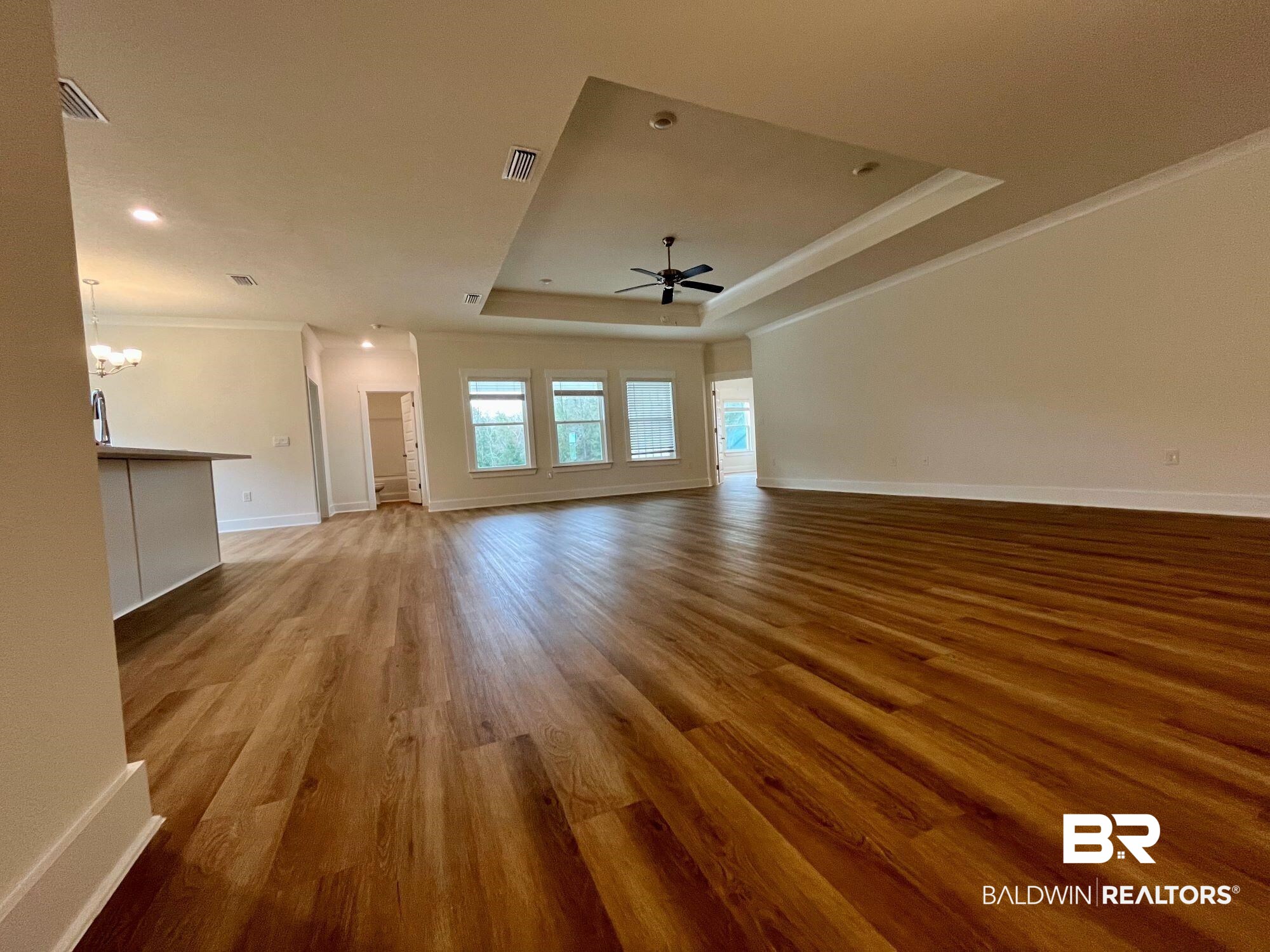 337 Barndling Street Fairhope, AL 36532 - Photo 11 of 34 Unfurnished living room with a tray ceiling, ceiling fan with notable chandelier, ornamental molding, and light hardwood / wood-style flooring