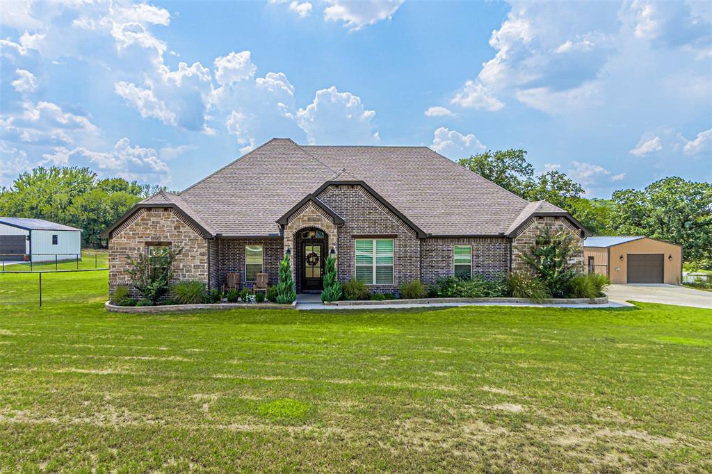 French country inspired facade with an outdoor structure, stone siding, brick siding, roof with shingles, and a garage