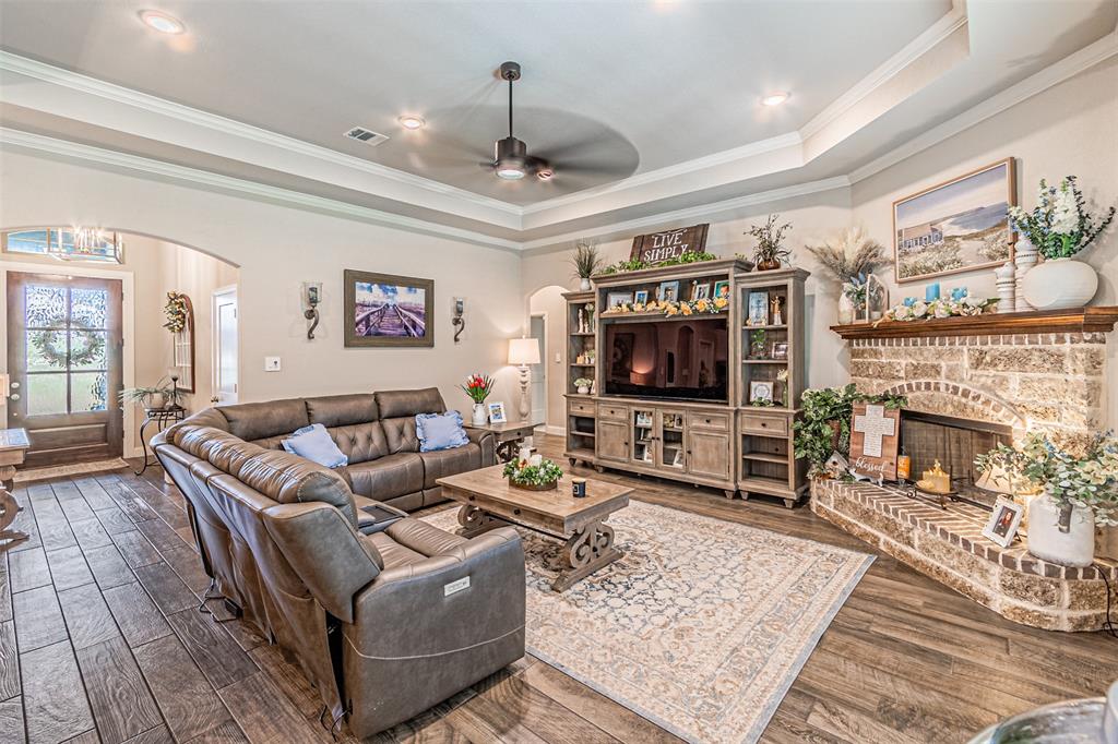 1009 Henry Way Springtown, TX 76082 - Photo 13 of 40 Living area with arched walkways, a raised ceiling, a ceiling fan, a brick fireplace, and ornamental molding
