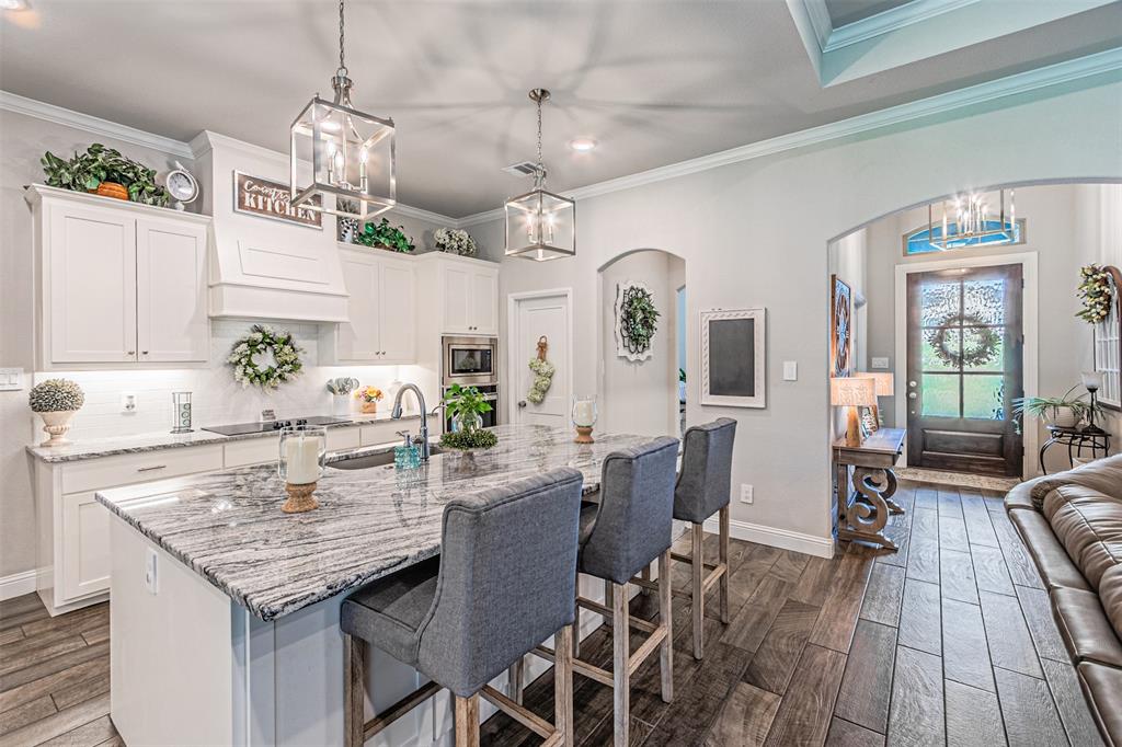 1009 Henry Way Springtown, TX 76082 - Photo 15 of 40 Kitchen featuring a chandelier, white cabinetry, dark wood-style flooring, a kitchen breakfast bar, and ornamental molding