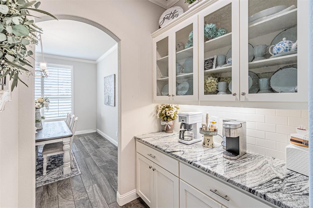 1009 Henry Way Springtown, TX 76082 - Photo 18 of 40 Bar area with arched walkways, crown molding, tasteful backsplash, light stone counters, and glass insert cabinets