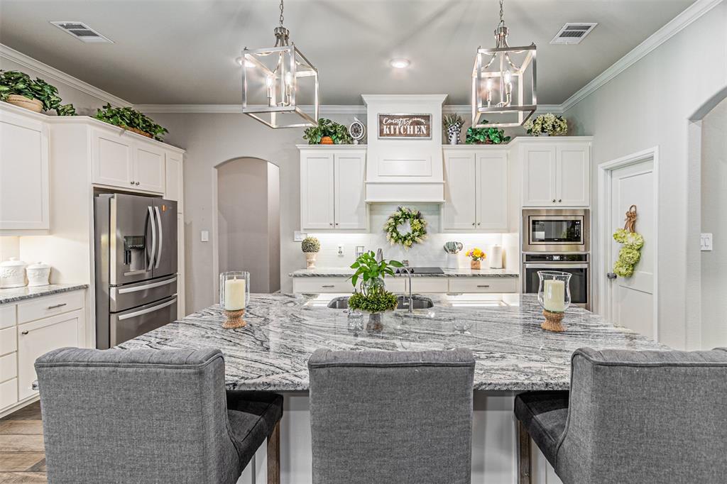 1009 Henry Way Springtown, TX 76082 - Photo 21 of 40 Kitchen with arched walkways, tasteful backsplash, white cabinets, light stone countertops, and crown molding