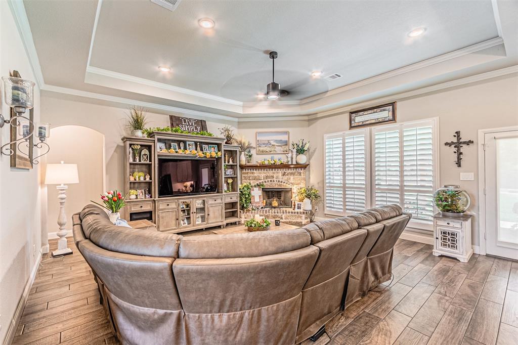 1009 Henry Way Springtown, TX 76082 - Photo 10 of 40 Living area featuring a tray ceiling, wood finished floors, ceiling fan, a brick fireplace, and crown molding