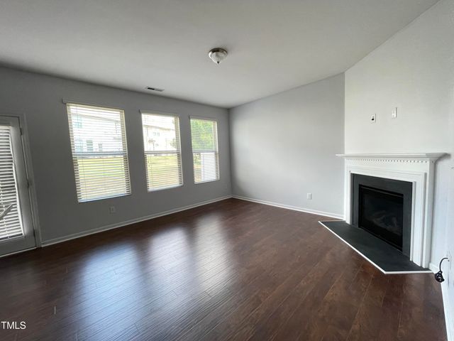 an empty room with wooden floor fireplace and windows