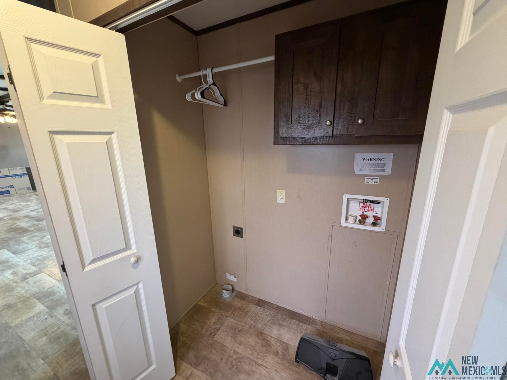 801 Riata Road Carlsbad, NM 88220 - Photo 27 of 39 Utility area featuring wood-finish flooring, a wall-mounted laundry hookup, and overhead cabinetry