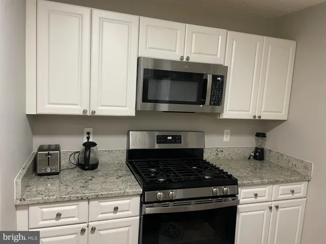 a kitchen with granite countertop white cabinets and a stove top oven
