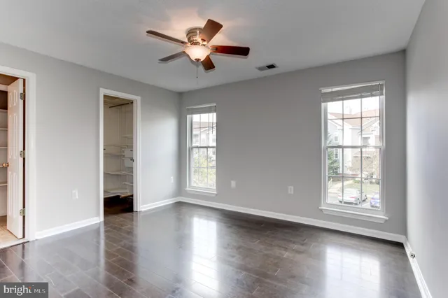 an empty room with wooden floor chandelier fan and windows