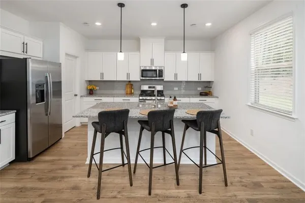 a kitchen with stainless steel appliances granite countertop a dining table chairs refrigerator and microwave