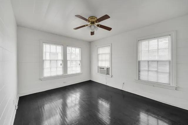 an empty room with wooden floor fan and windows