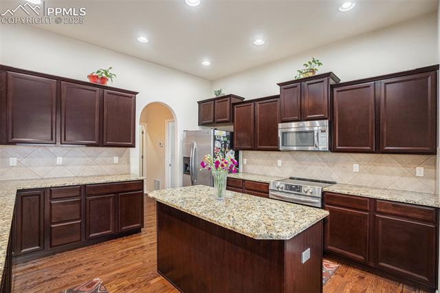 9709 Rockingham Drive Peyton, CO 80831 - Photo 12 of 50 Kitchen featuring stainless steel appliances, arched walkways, wood finished floors, a kitchen island, and backsplash
