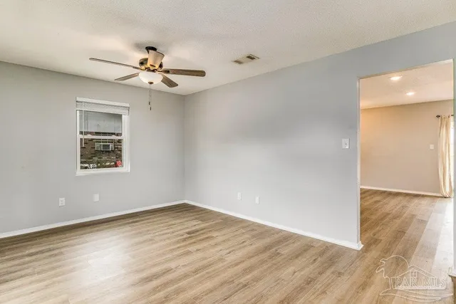 an empty room with wooden floor fan and windows