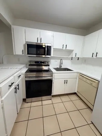 a white kitchen with granite countertop a stove top oven microwave and cabinets