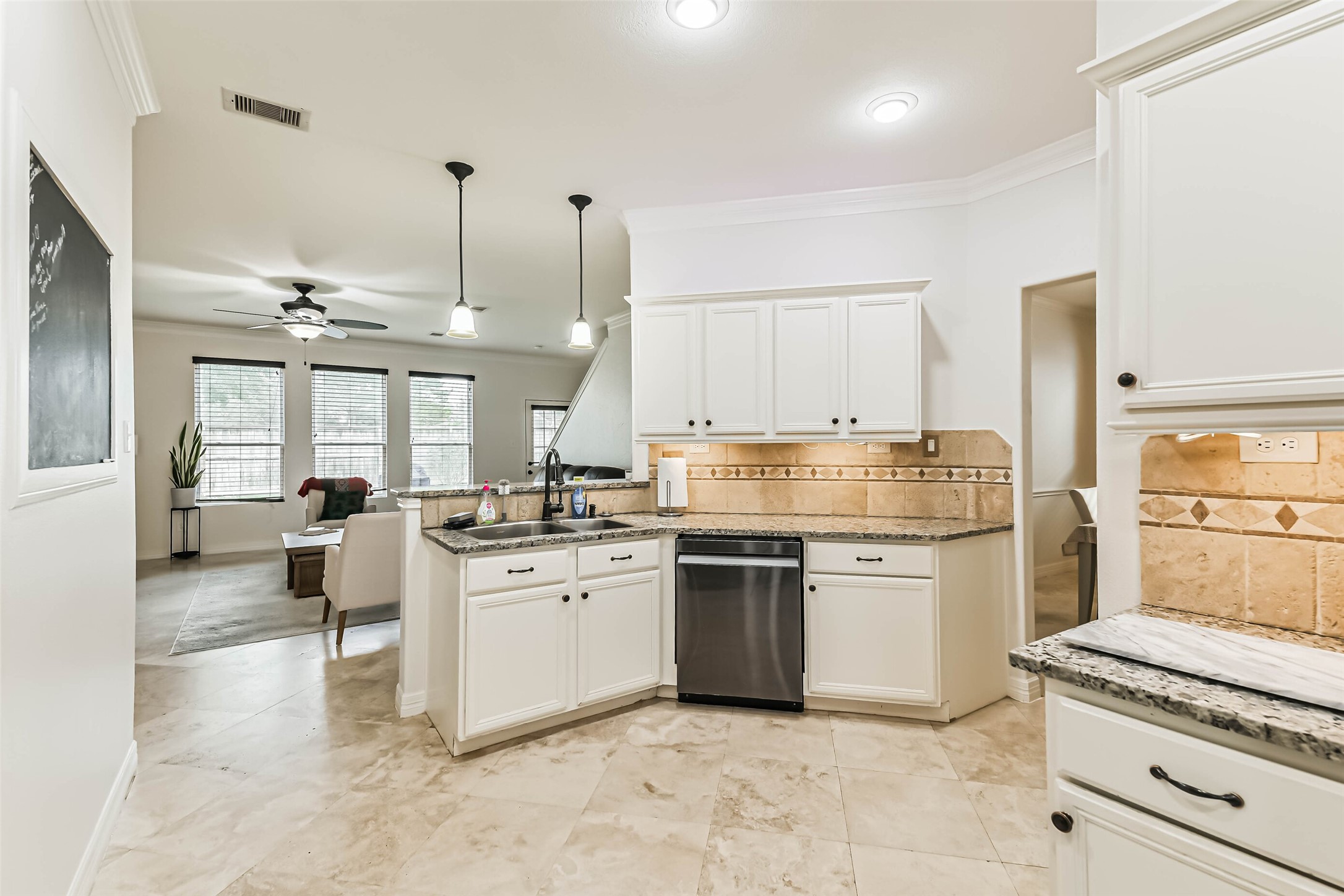 This bright, open-concept kitchen features granite countertops, stainless steel appliances, and ample cabinetry. It flows seamlessly into a cozy living area with large windows and tile flooring, perfect for entertaining.