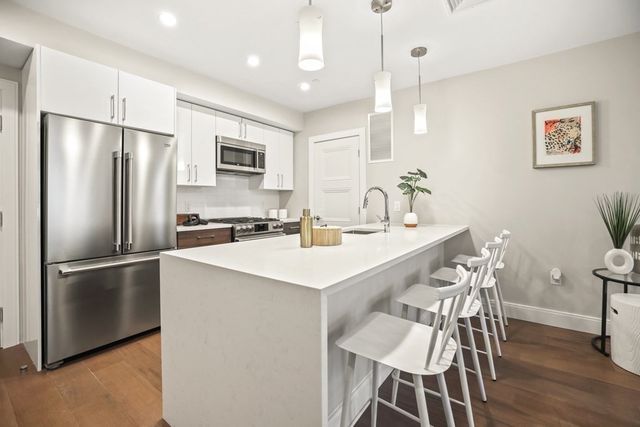 a kitchen with stainless steel appliances a refrigerator a stove a dining table and chairs with wooden floor