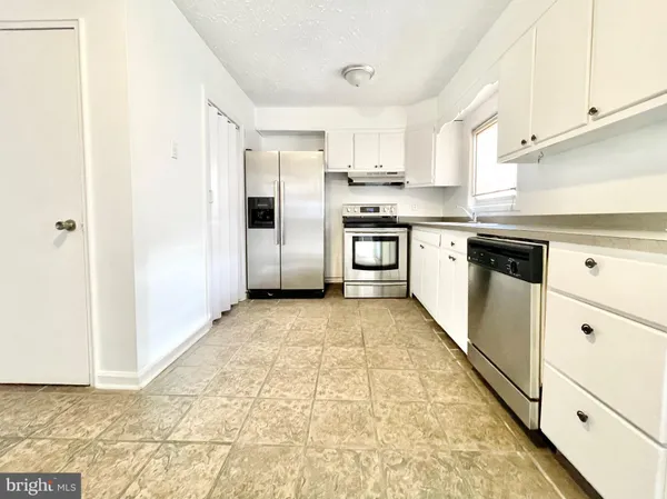 a kitchen with granite countertop a refrigerator and white cabinets