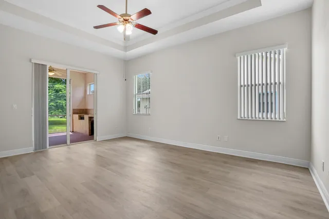 an empty room with wooden floor chandelier fan and windows