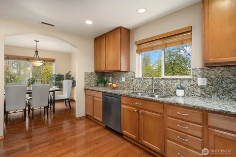 a kitchen with stainless steel appliances granite countertop wooden cabinets a sink dishwasher a stove and a refrigerator with wooden floor