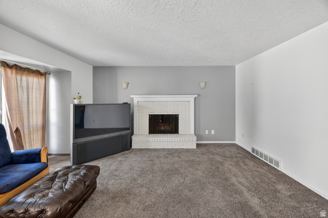 1218 East 100 South Logan, UT 84321 - Photo 12 of 23 Living area featuring a brick fireplace with a painted white mantel, gray accent wall, and neutral tone carpeting