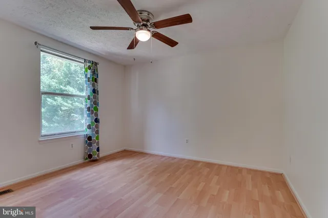 an empty room with wooden floor fan and windows