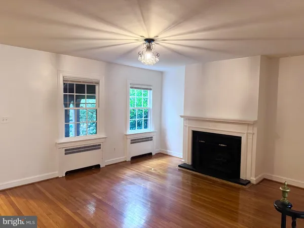 a view of an empty room with wooden floor and kitchen view