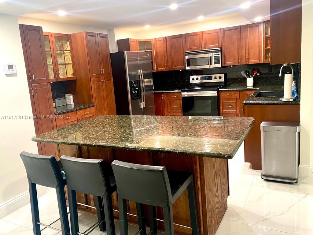 a kitchen with stainless steel appliances kitchen island granite countertop a table chairs and microwave