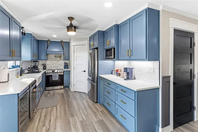 a kitchen with stainless steel appliances granite countertop a refrigerator a sink dishwasher a stove and white countertops with wooden floor