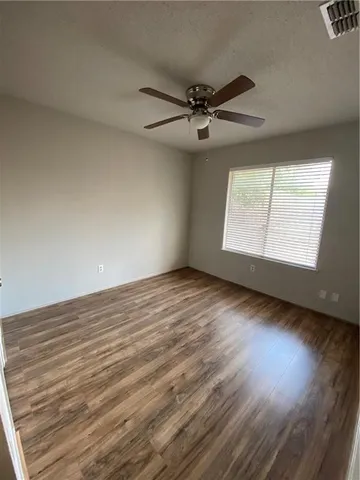 an empty room with wooden floor fan and windows