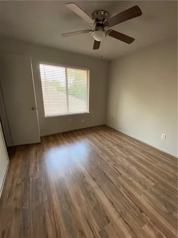 an empty room with wooden floor chandelier fan and windows