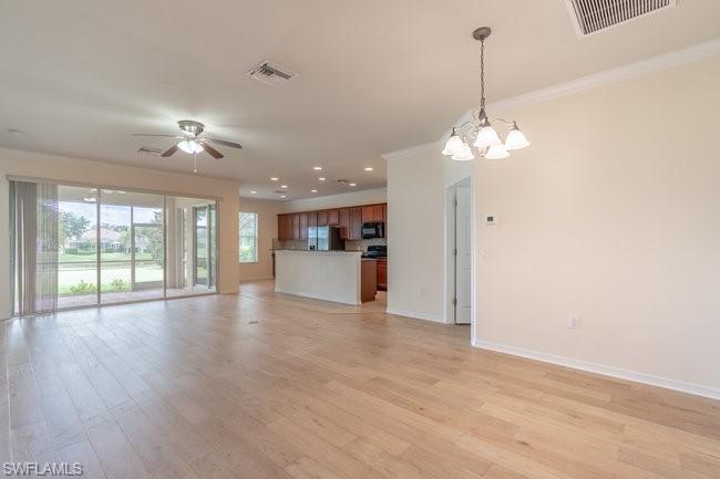 Unfurnished living room featuring ceiling fan with notable chandelier, light hardwood / wood-style floors, and ornamental molding