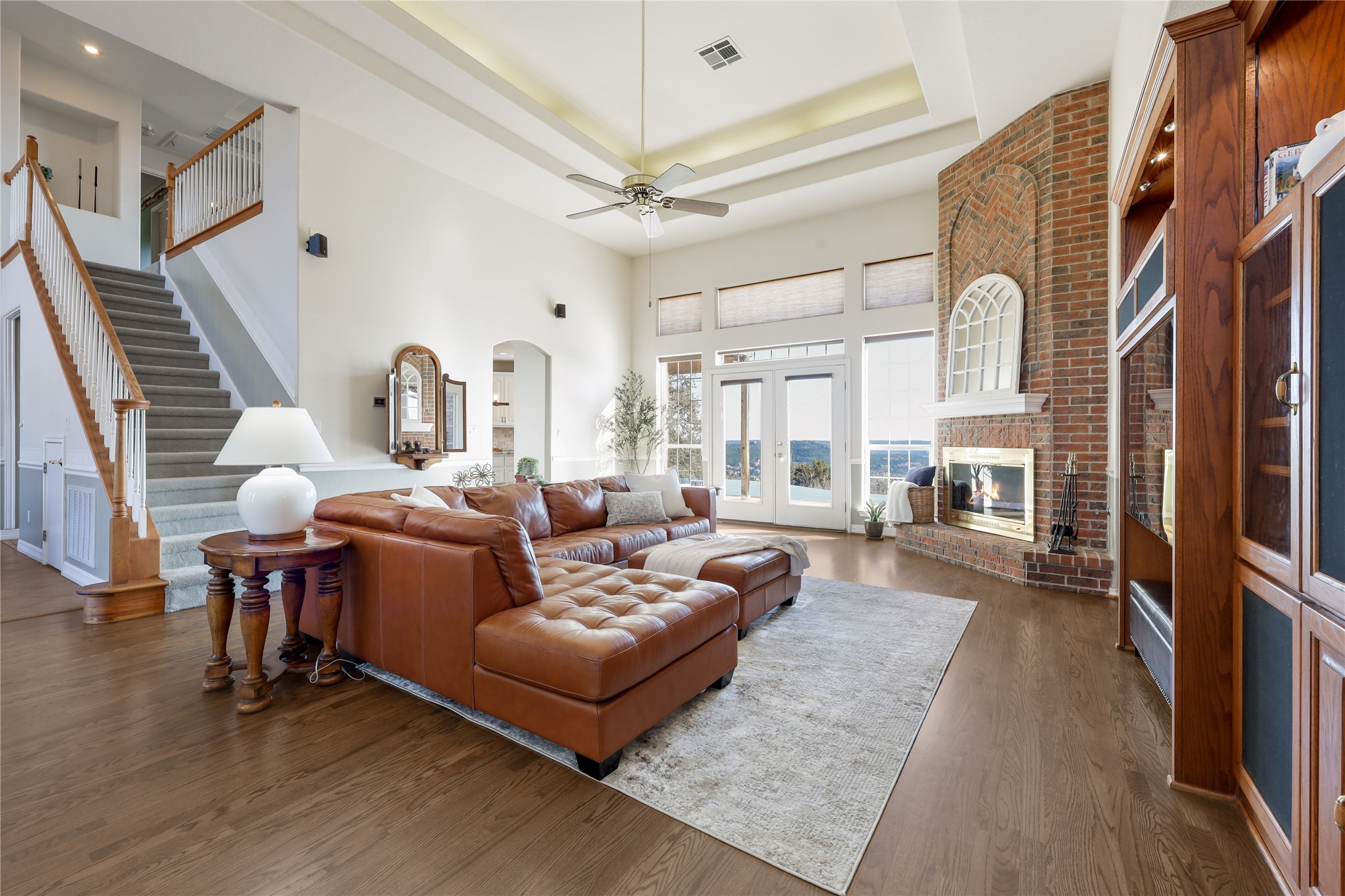 18607 White Rim Trail Jonestown, TX 78645 - Photo 8 of 40 Living room featuring a brick fireplace, arched walkways, dark wood-style flooring, a ceiling fan, and a tray ceiling