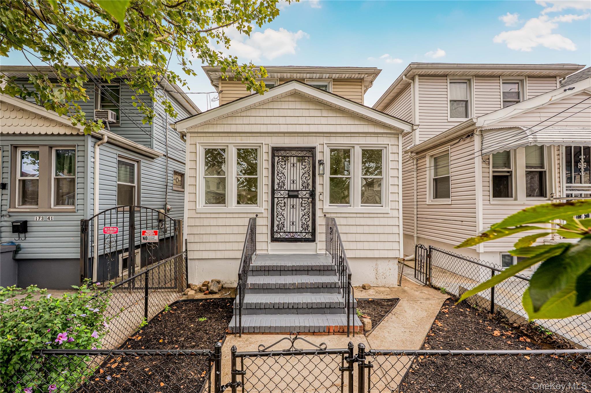 173-43 103rd Road Queens, NY 11433 - Photo 41 of 43 Siding exterior with multiple windows, leading to a front entry with a security door, and a paved walkway