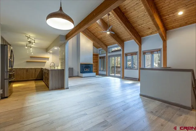 a view of an empty room with wooden floor and a kitchen