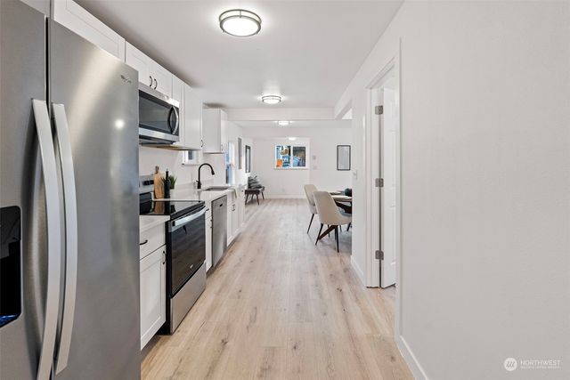 a kitchen with stainless steel appliances a refrigerator a sink a stove and white cabinets with wooden floor