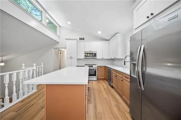 a large kitchen with stainless steel appliances kitchen island granite countertop a refrigerator a stove a sink dishwasher and white cabinets with wooden floor