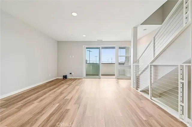 a view of empty room with wooden floor and kitchen view