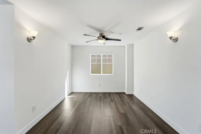 an empty room with wooden floor chandelier fan and windows