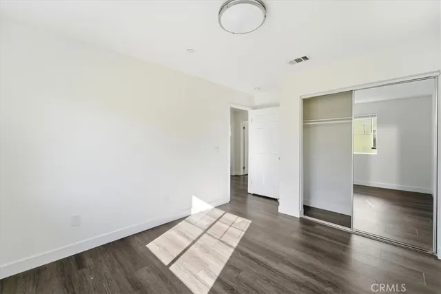 a view of an empty room with wooden floor and closet