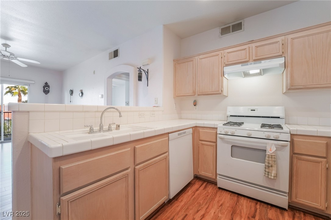 2201 Ramsgate Drive, Unit 823 Henderson, NV 89074 - Photo 10 of 31 Kitchen featuring white appliances, visible vents, a peninsula, light brown cabinetry, and under cabinet range hood