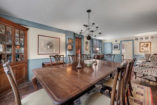 a view of a dining room and livingroom with furniture wooden floor a rug a painting and a chandelier