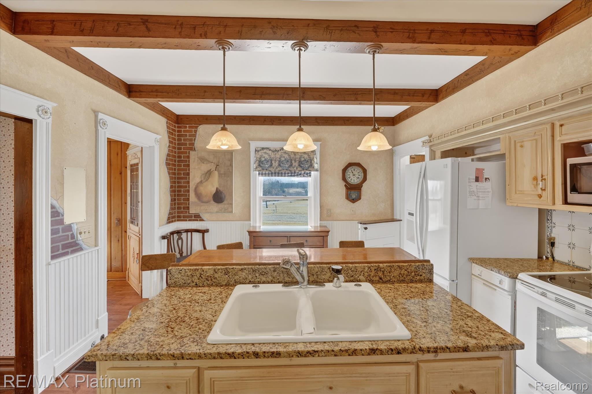 15330 Howlett Road Gregory, MI 48137 - Photo 4 of 26 Kitchen featuring wainscoting, white appliances, light wood finish cabinets, an island with sink, and decorative light fixtures