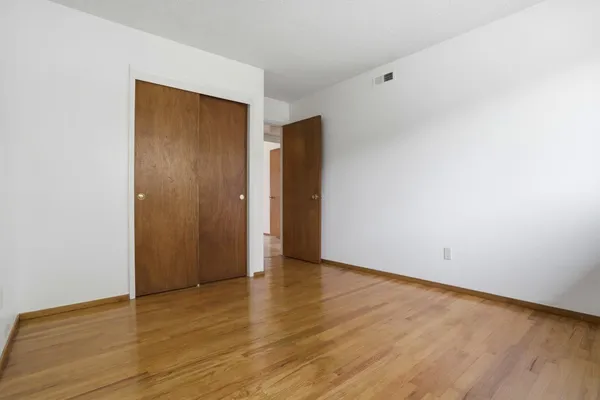a view of an empty room with wooden floor and closet